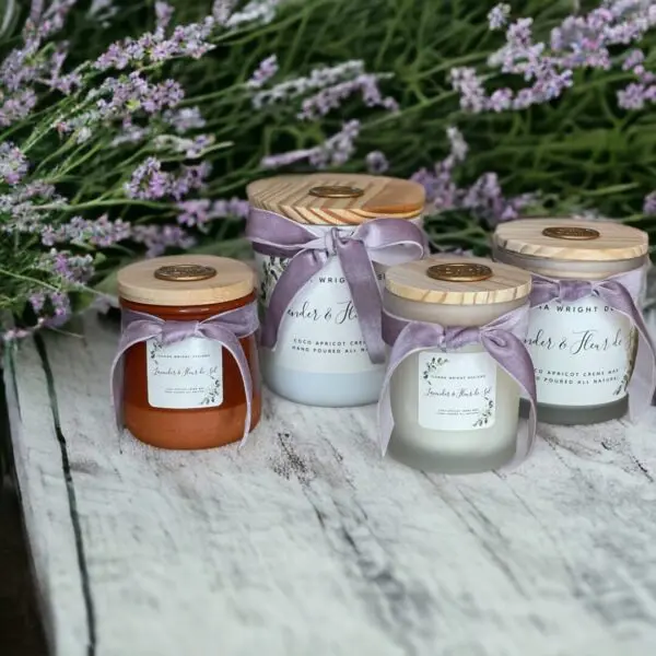 Four of the best lavender scented candles in the Lavender & Fleur de Sel candle collection by Donna Wright Designs with wood lids and purple velvet ribbon in frosted glass containers sitting on a wood table with fresh lavender in the background.