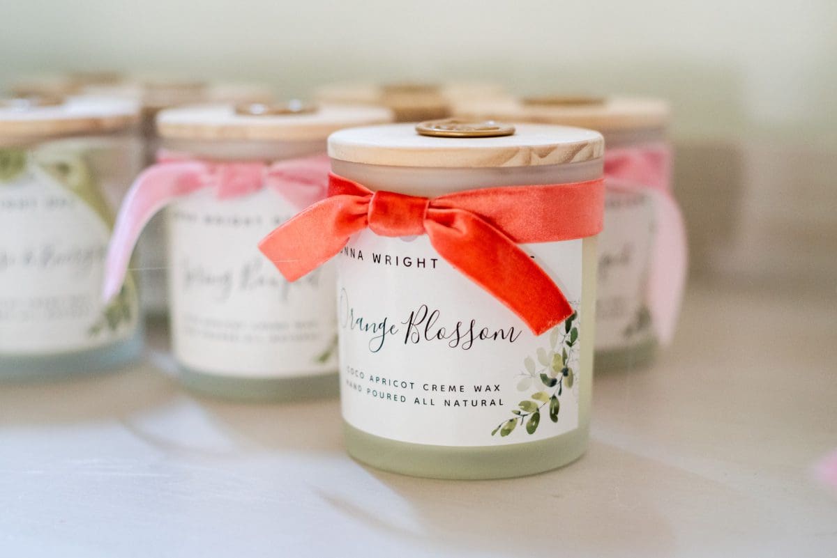 Donna Wright Designs A close-up of a Signature Scent Subscription candle jar with a label that reads "spring blossom" tied with a pink ribbon, surrounded by other similarly styled Signature Scent Subscription candle jars.