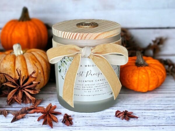 Harvest Pumpkin Spice Candle with wooden wick 12 oz by Donna Wright Designs using coco apricot creme wax, candle with wooden wick in frosted glass vessel, wood lid and velvet ribbon sitting on a white wood table with pumpkins in the background.