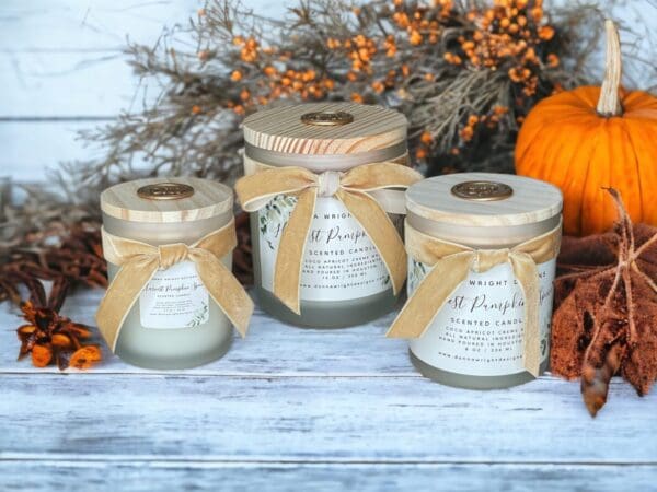 Harvest Pumpkin Spice candles by Donna Wright Designs, the best Pumpkin candles with wooden wicks made from coco apricot creme wax and all natural ingredients in frosted glass vessels with wood lids embellished with velvet ribbon sitting on a white wood table with pumpkins in the background.