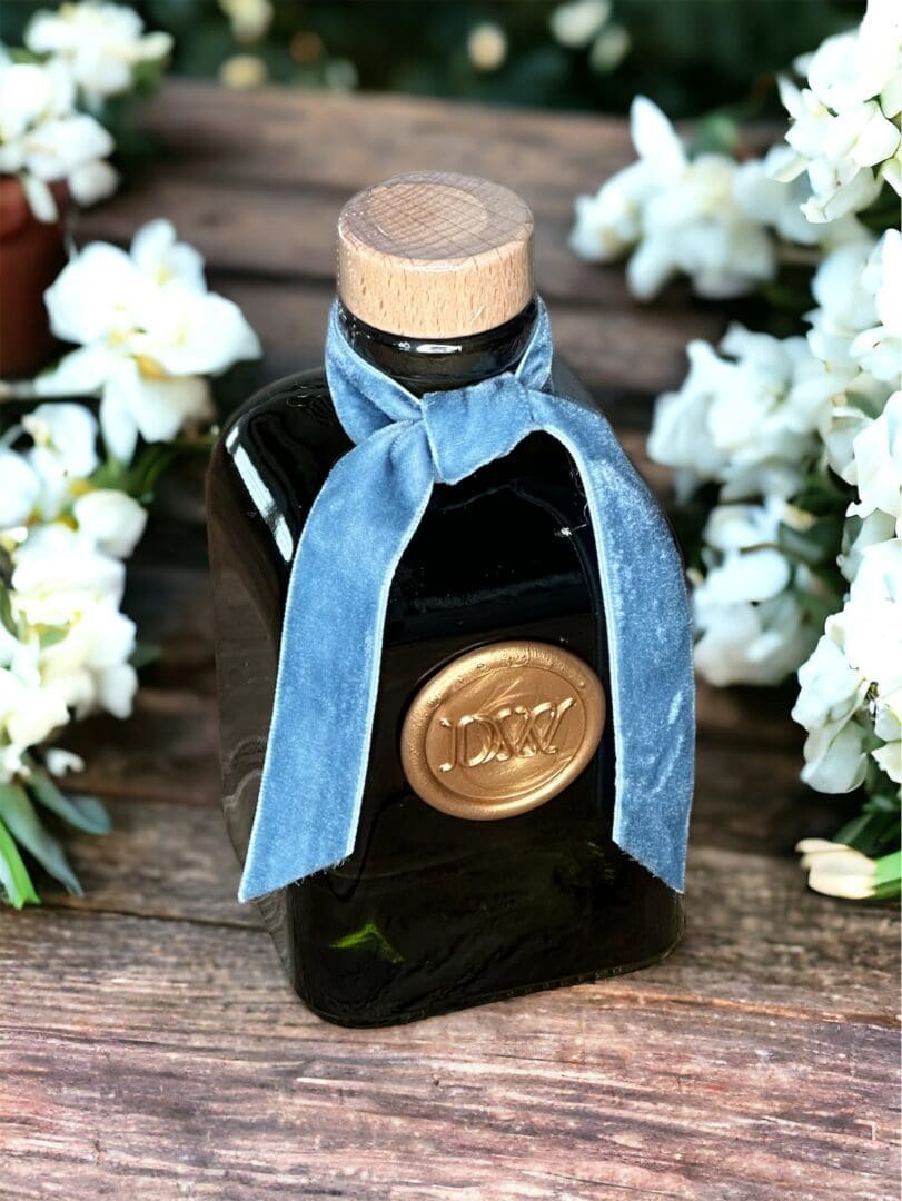 Donna Wright Designs Gardenia & Tuberose Diffuser - 6 with a blue ribbon around its neck and a gold seal, surrounded by white gardenias on a wood table.