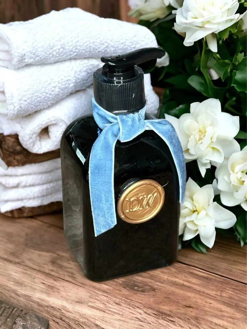Donna Wright Designs An elegant Gardenia & Tuberose Diffuser - 6 Oz adorned with a gold seal and a blue ribbon, surrounded by white gardenia, against a soft background.