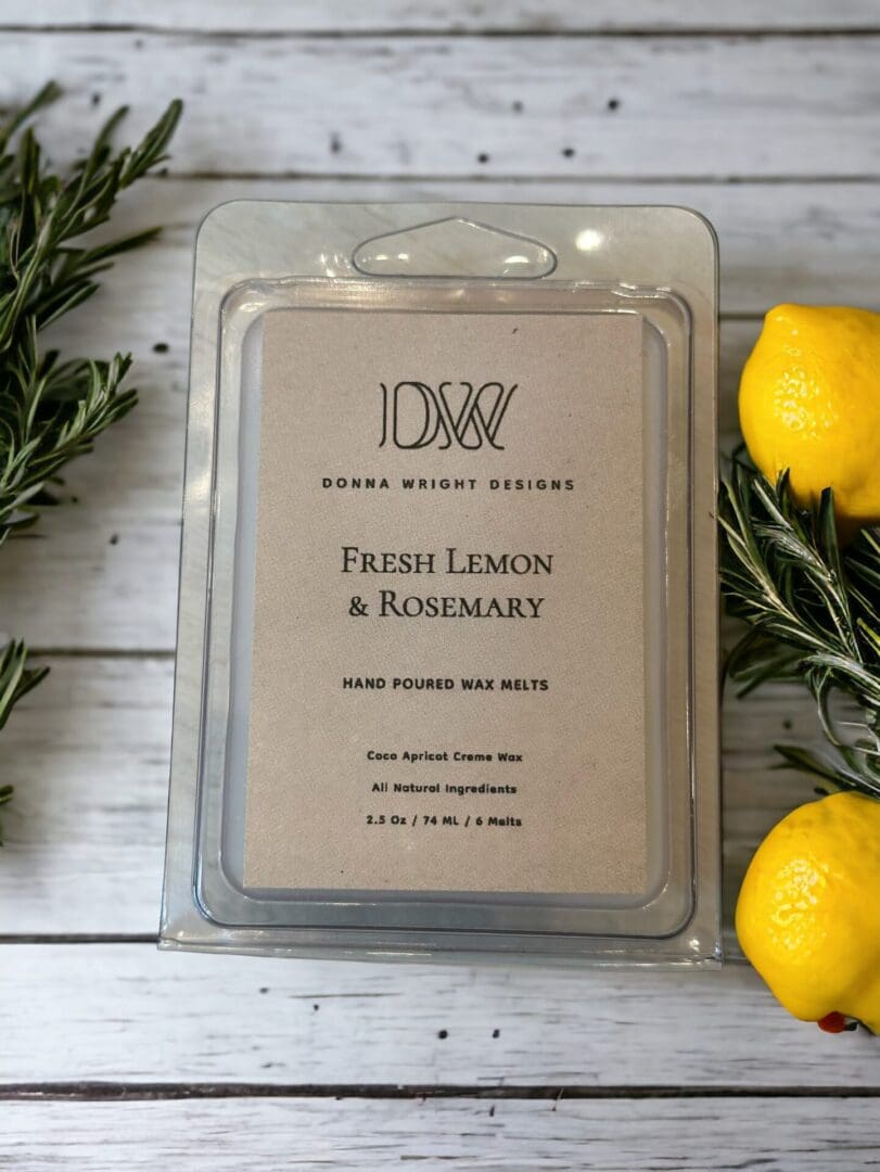 Donna Wright Designs A package of Fresh Lemon & Rosemary Wax Melts on a wooden surface, surrounded by rosemary sprigs and fresh lemons.
