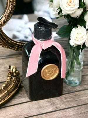 Spring Bouquet hand soap by Donna Wright Designs, all natural ingredients in a vintage green pump bottle with a gold seal and pink ribbon, placed on a wooden surface next to white roses