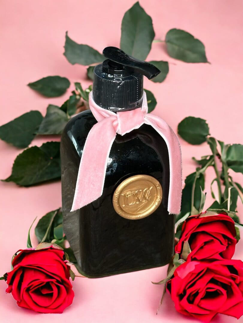 Donna Wright Designs A black bottle with a pink ribbon and a gold seal, surrounded by red roses on a pink background, resembling the Spring Bouquet - Medium Gift Basket.