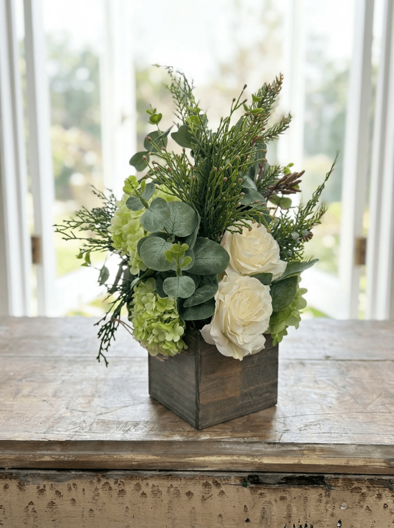 The Small Floral in Wood Box features white roses, green hydrangeas, eucalyptus leaves, and assorted greenery for a charming rustic display.